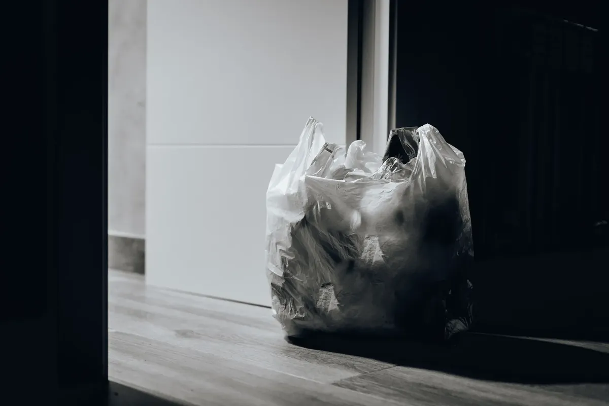 暗い部屋にプラスチック袋に trash が詰まっている、廃棄物とリサイクルを強調している。