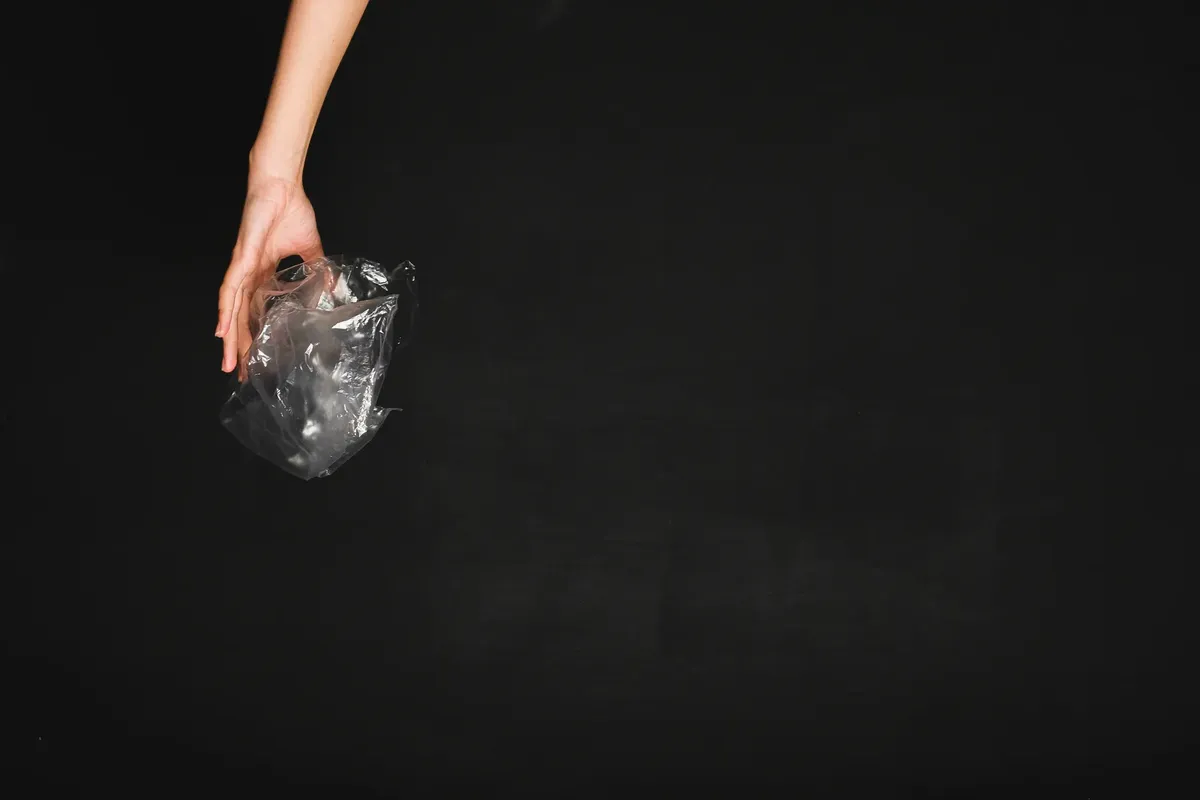 手が黒い背景に透明なプラスチック袋を押し当てている、汚染とリサイクルを象徴している。