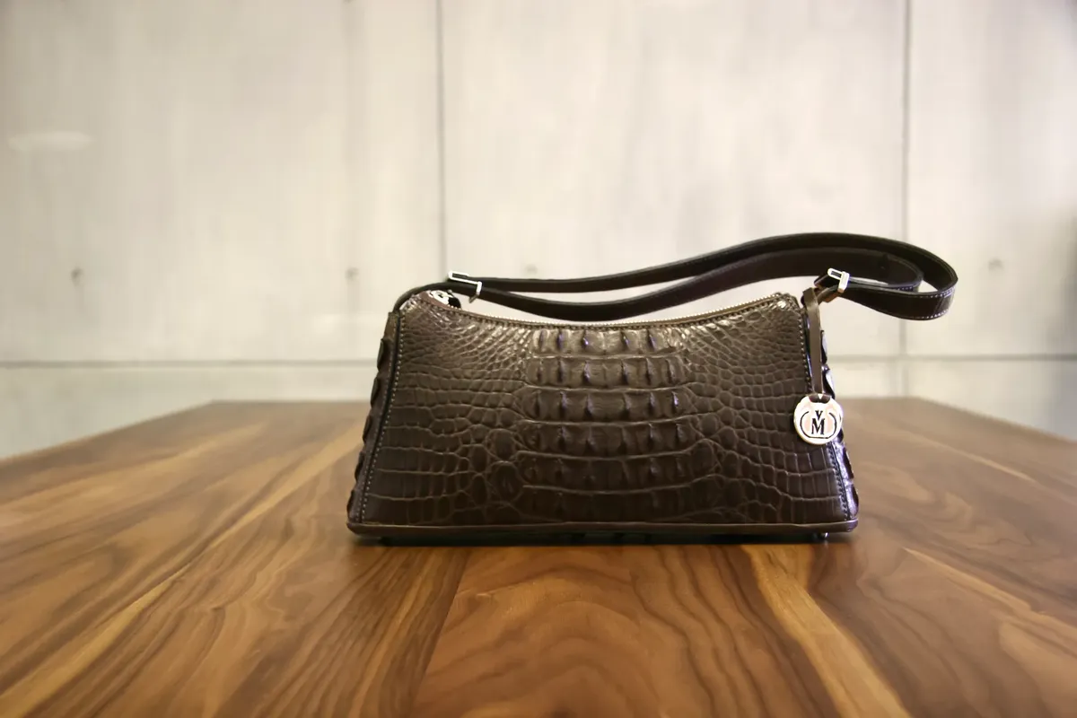 Elegant crocodile leather handbag elegantly placed on a wooden table with a modern backdrop.