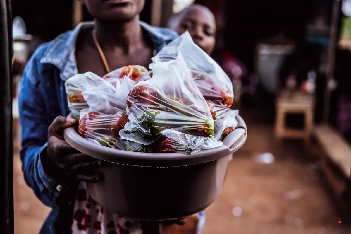 Woman selling fresh vegetables in plastic bags at outdoor market, showcasing local trade.