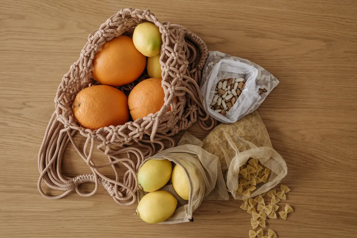 Eco-friendly grocery with fruits, pasta, and beans in reusable mesh bags on wooden surface.