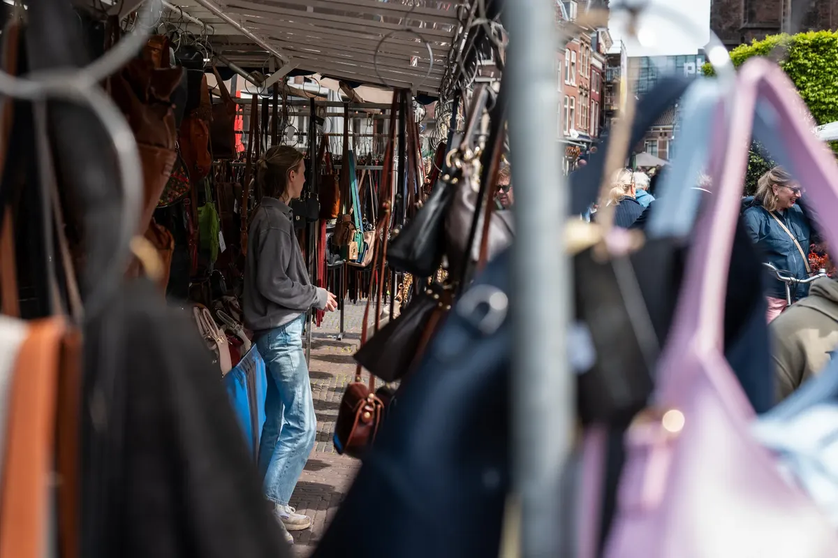 Shoppers browse leather goods at an outdoor market on a sunny day.