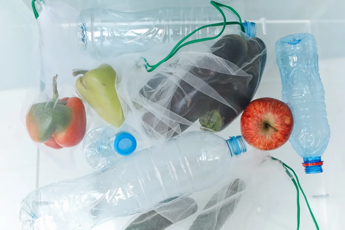 再利用可能なネット袋にプラスチックボトルと野菜が入っていて、エコフレンドリーな買い物を促しています。